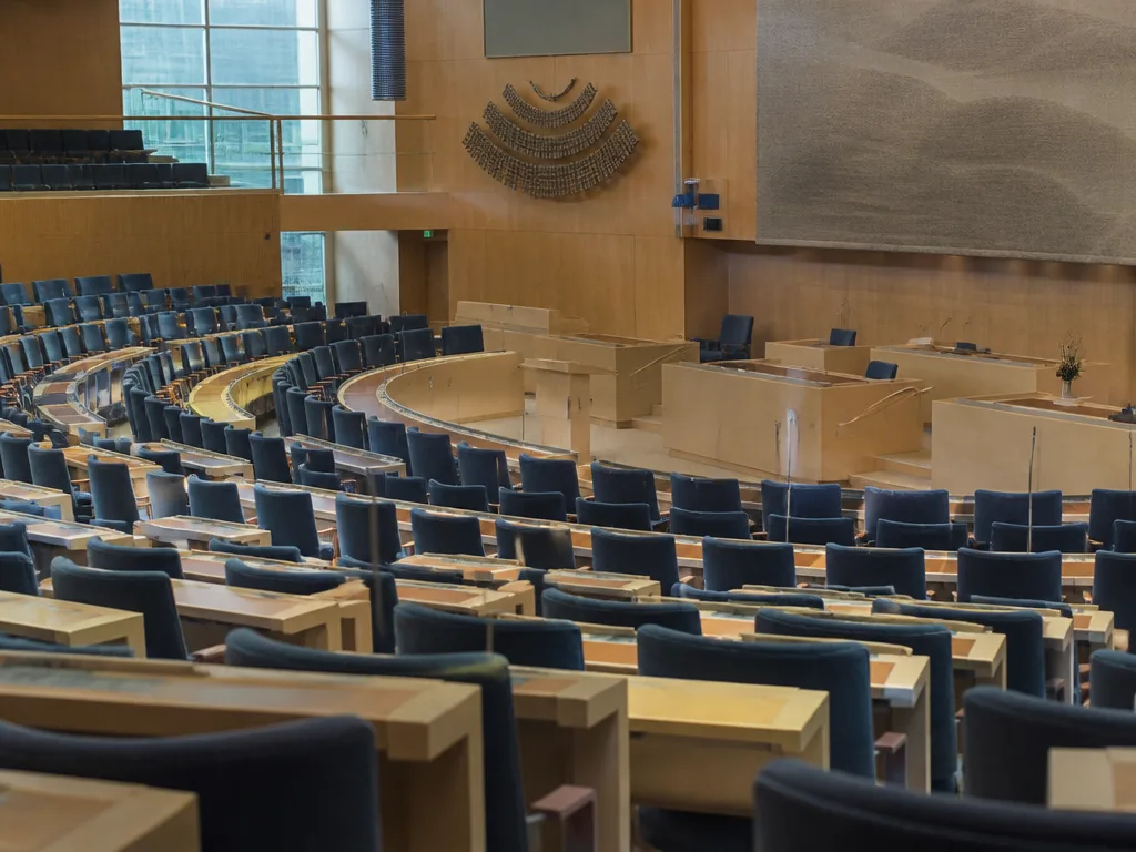 Tom kammarsal i riksdagen med bänkrader och talmannens podium i mjukt ljus